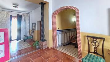 A spacious hallway with a tiled floor, a brick column, a bench, and a door leading to another room.