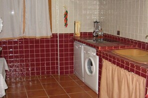 Cozinha compacta com máquina de lavar, pia e paredes revestidas de azulejos.