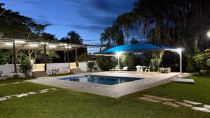 Ein Swimmingpool mit blauer Markise, umgeben von einer Steinterrasse und einem Rasen.