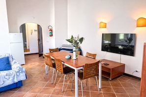 A compact living space with a dining table, chairs, a sofa, a TV, and a small kitchen area.