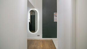 A hallway with a wooden floor, a dark door with a sign, and a wall-mounted light fixture.