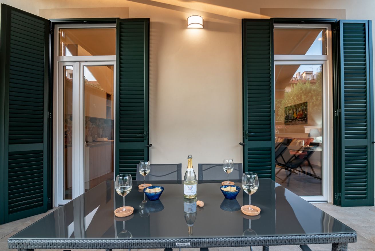 Ein Tisch mit Glasplatte, vier Weingläsern, einer Flasche Weißwein und blauen Schalen mit Snacks.