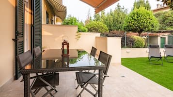 Un patio con un tavolo e sedie in vetro, un lanterne e un prato verde.