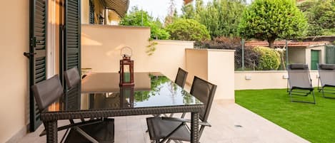 Un patio con una mesa y sillas de vidrio, un farol y un césped verde.