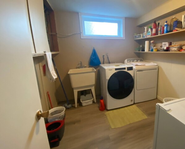 Een wasserette met een wasmachine, droger, wastafel en een raam.