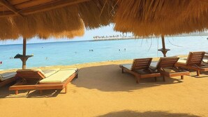 A beach with thatched umbrellas, wooden lounge chairs, and a clear view of the sea.