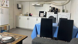 A compact kitchen with a washing machine, a coffee maker, and a dining area with a table and chairs. - Basement Apartment in Villa (Odense)