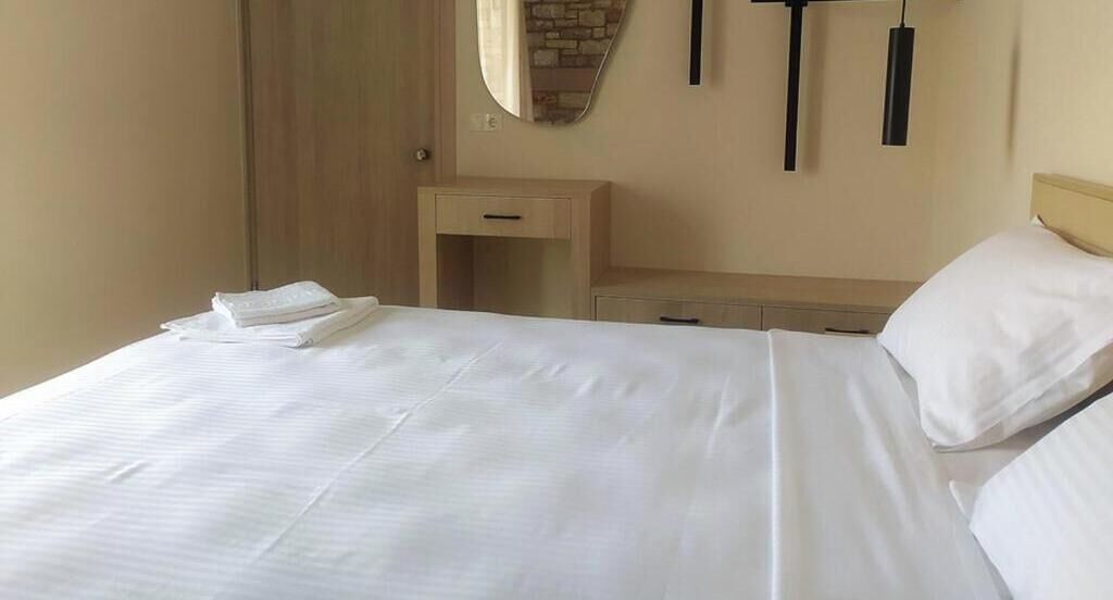 Et hotelværelse med en seng, et natbord, et spejl og en lampe på væggen.