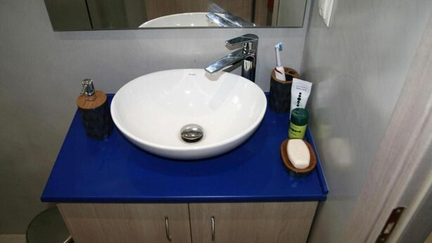 Un baño con lavamanos blanco, encimera azul y un espejo encima.