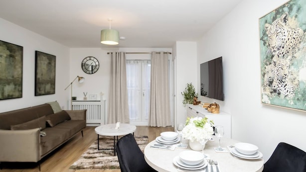 Ein modernes Wohnzimmer mit einer Couch, einem Esstisch für vier Personen und einem an der Wand befestigten Fernseher.