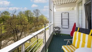 Un balcone con vista su alberi e un edificio bianco. Si nota una sedia a righe gialle e bianche e un tavolino.