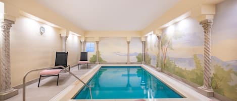 Une piscine ornée d’une fresque murale, de colonnes et de chaises longues.