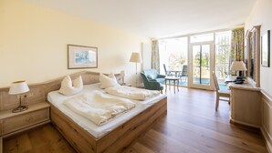 Una camera da letto con un letto di legno, un comodino, una scrivania, una sedia e vista sull'esterno attraverso una grande finestra.