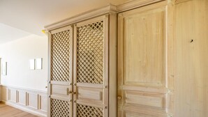 Un corridoio con pavimento in legno, parete bianca e una porta chiusa in legno con decorazioni a griglia.