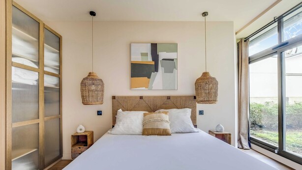 A bed with a wooden headboard, two bedside tables, a hanging abstract painting, and a large window with a view. - Spacious Apartment - 2BR/10P - Place d'Italie (Paris)
