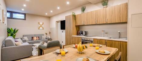 Une cuisine moderne avec des meubles en bois, une table à manger dressée pour le petit-déjeuner et un coin salon avec un canapé et des plantes.