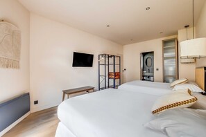 Ein Hotelzimmer mit zwei Betten, einem Fernseher, einem Kleiderschrank, einem Schreibtisch und einem Badezimmer.