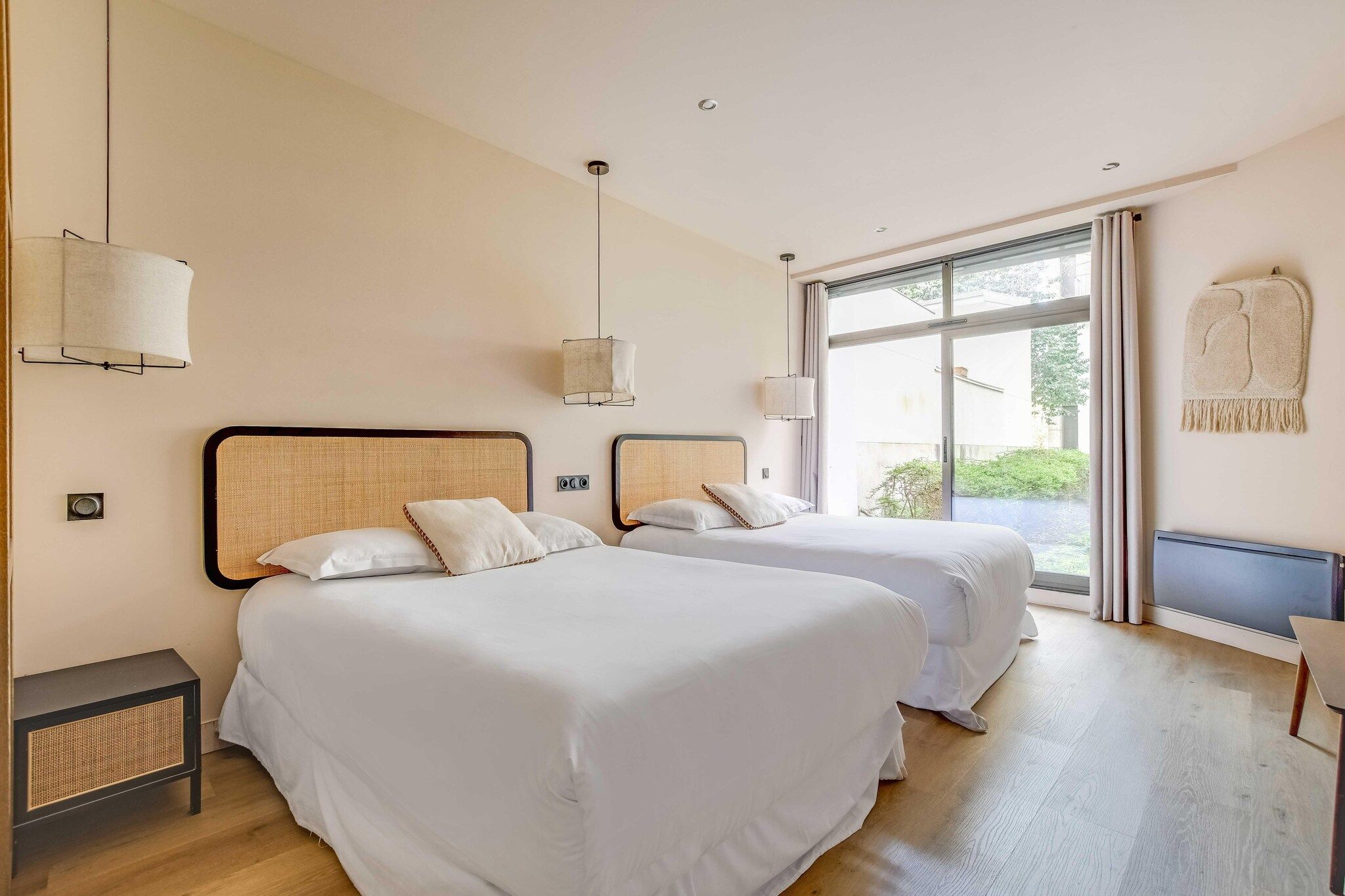 A hotel room with two beds, a small table, and a window with curtains.
