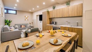A modern kitchen with wooden cabinets, a dining table set with plates, glasses, and a fruit bowl. - Spacious Apartment - 2BR/10P - Place d'Italie (Paris)