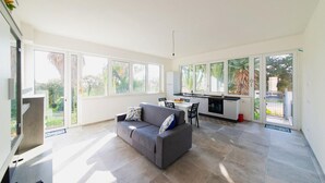 A spacious living area with a grey sofa, a dining table, and a kitchen area. - Holiday Home in 	Mazara del Vallo (Mazara del Vallo (TP))