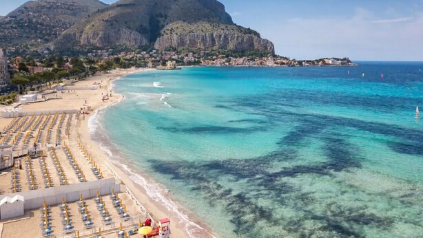 A coastal beach with rows of sun loungers and umbrellas, a clear blue sea, and a mountain in the background. - Holiday Home in 	Mazara del Vallo (Mazara del Vallo (TP))
