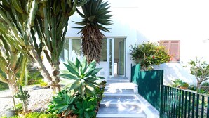 A modern house with a white exterior, a green fence, and a variety of plants including cacti and a tree with red flowers. - Holiday Home in 	Mazara del Vallo (Mazara del Vallo (TP))