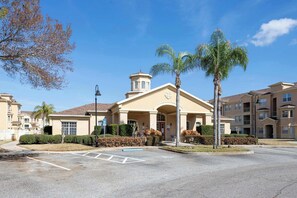 A building with a central entrance, a small tower, and a parking lot with marked spaces. - 3BR Condo with Pool View & Gym Near Disney (Davenport)