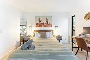 Habitación de hotel con una cama grande, un escritorio con silla, televisión y un cuadro con cactus en la pared.