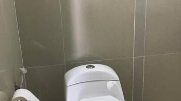 Een toilet met een witte spoelhendel en een papieren handdoekhouder aan de muur.