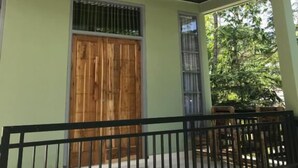 A building with a light green exterior, a wooden door, and a black railing in front. - Pohon Purba Resort & Restaurant (Labuhan Lombok)