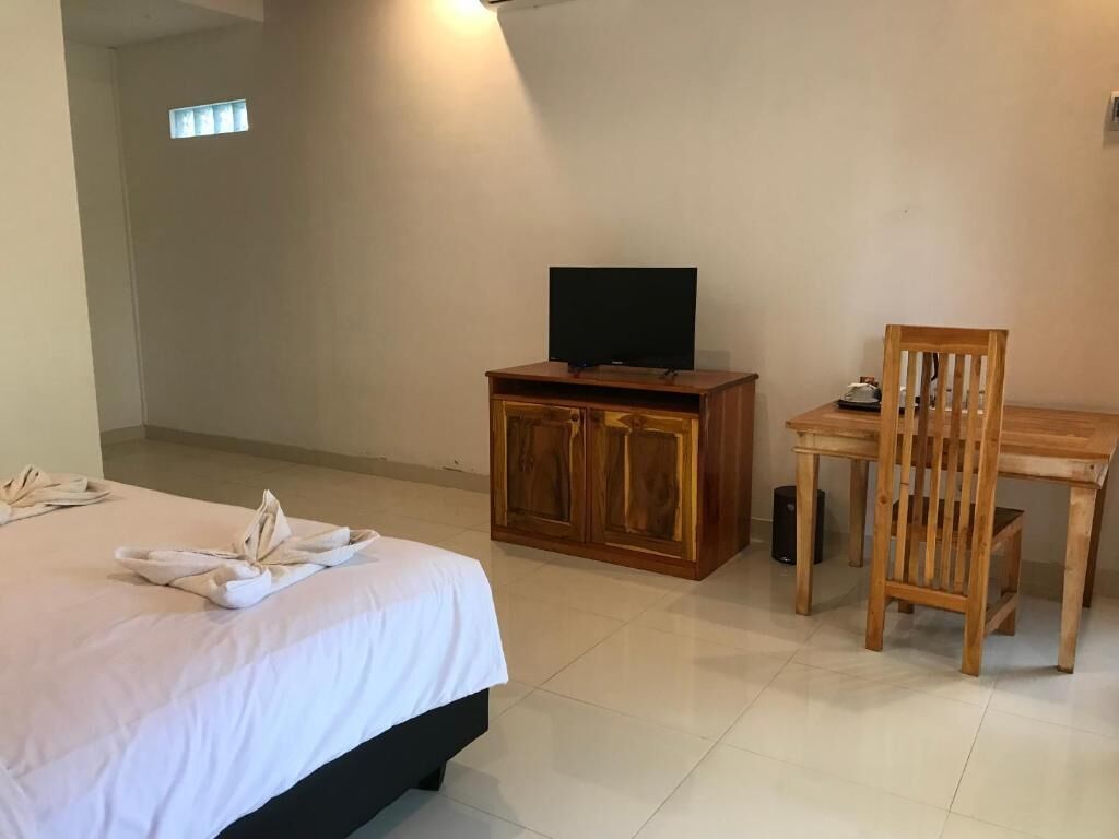 A hotel room with a bed, a television on a wooden cabinet, a dining table with a chair, and a small window.
