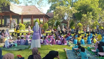 Une réunion en plein air où les participants sont assis sur l’herbe, certains sont debout, et on aperçoit une structure en arrière-plan.