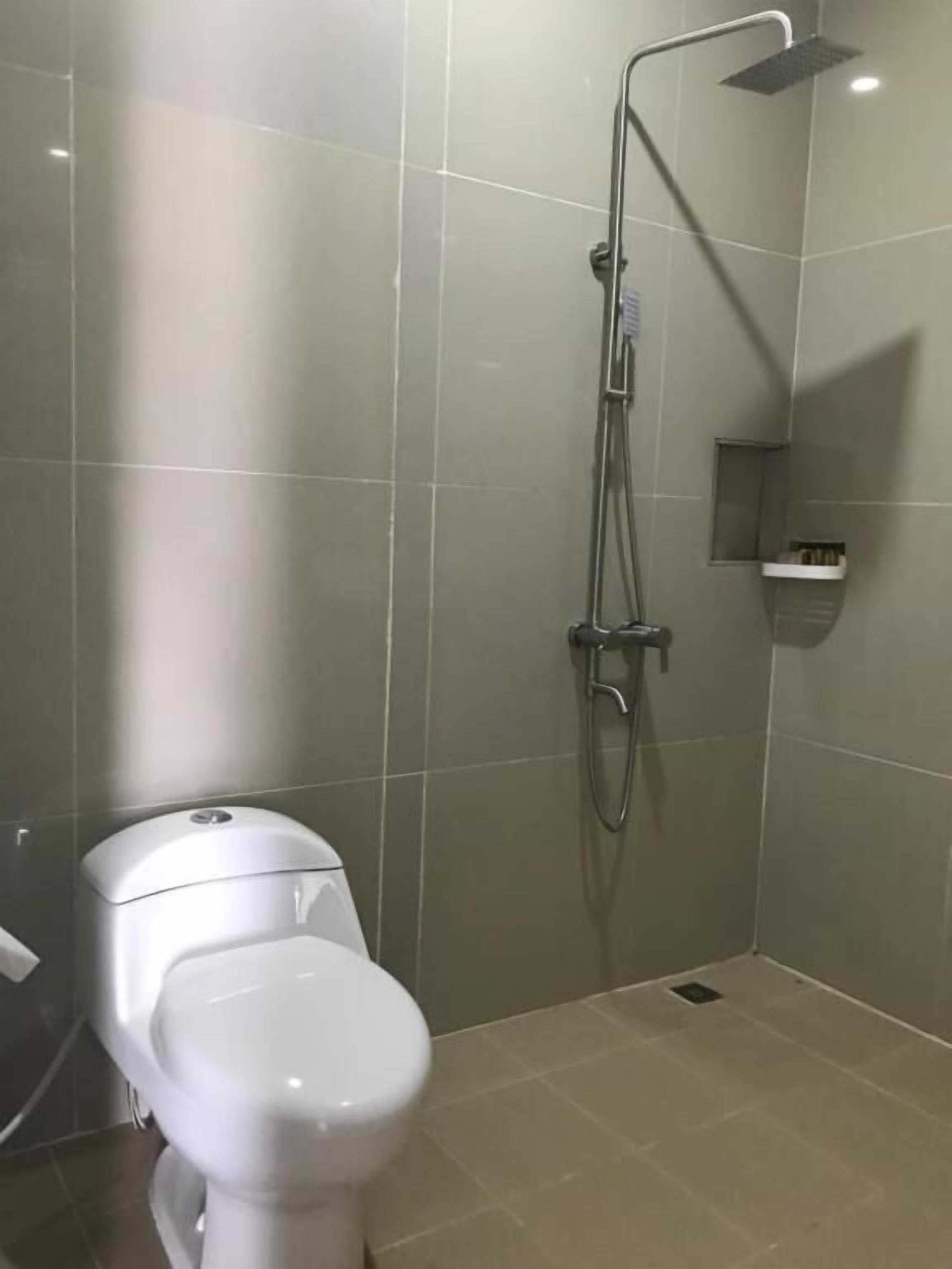 Un baño moderno con inodoro, ducha con cabezal de ducha manual y un estante pequeño.