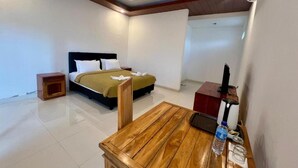 A hotel room with a bed, a wooden table, a nightstand, and a desk with a computer. - Pohon Purba Resort & Restaurant (Labuhan Lombok)