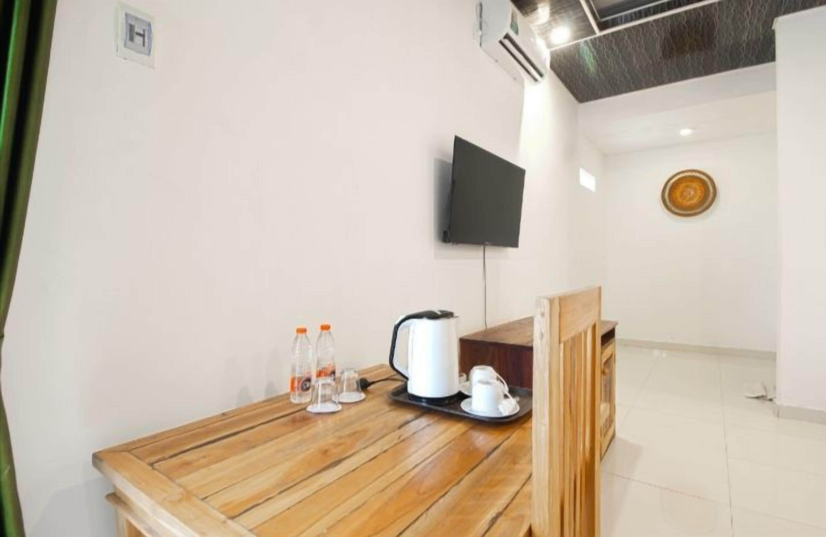 Une table en bois avec une bouilloire, des tasses et des bouteilles, un téléviseur accroché au mur et une assiette décorative également fixée au mur.