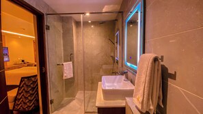 A modern bathroom with a glass-enclosed shower, a white sink, and a large mirror. - Urbanwoods Hotel Suites by icon (Nairobi)