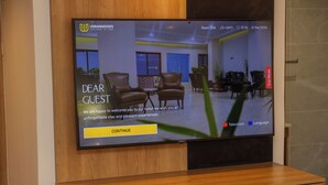 En hotellreception med en tv-skärm som visar ett välkomstmeddelande, ett träskåp under skärmen och en växt i förgrunden.