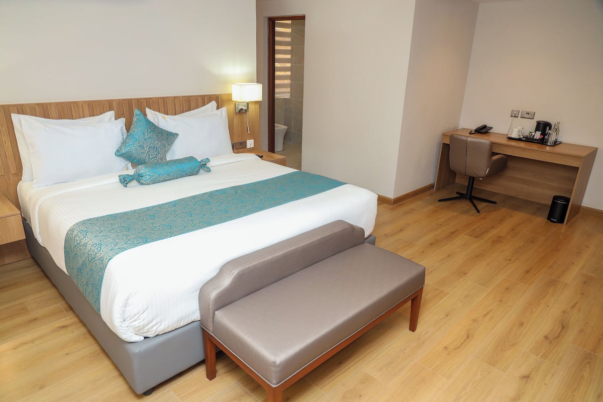 A hotel room with a bed, a desk, a bench, and a shower area.