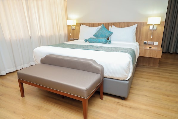 A hotel room with a bed, bedside tables, a bench, and a nightstand. - Urbanwoods Hotel Suites by icon (Nairobi)