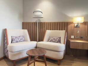 A modern hotel room with two sofas, a small wooden table, a floor lamp, and a bedside table with a lamp. - Urbanwoods Hotel Suites by icon (Nairobi)