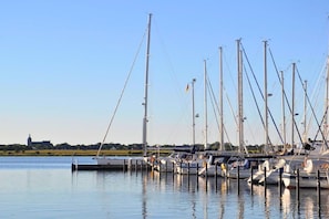 A marina with multiple sailboats docked, a clear sky, and a distant building. - Ferienwohnung Am Yachthafen mit Balkon (Fehmarn OT Burgtiefe-Südstrand)
