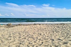 Une plage de sable où l’on peut voir des empreintes menant à l’eau, un ciel dégagé et une mer calme.