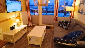 Una habitación acogedora con sofá, una mesita, televisión y ventana con cortinas.