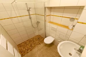 Une salle de bain avec douche, toilettes, lavabo et carrelage au sol.