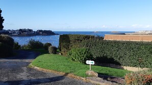 A coastal road with a D-shaped sign, a grassy area, and a view of boats on the water.