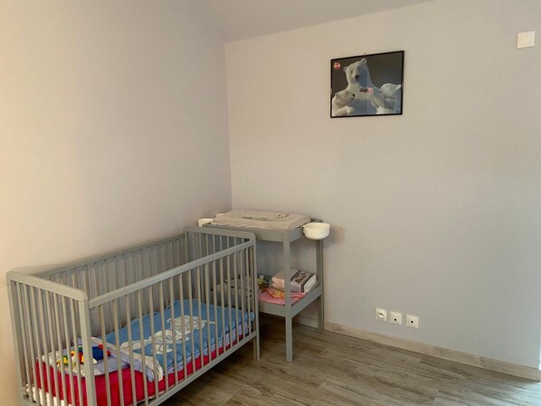 A baby crib with a changing table beside it, a small shelf with books, and a framed picture on the wall.