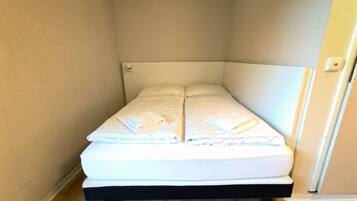 A small, single-bed room with a white headboard and a neatly made bed.