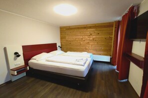 Une chambre à coucher avec une tête de lit en bois, un lit recouvert de draps blancs, une table de chevet et un téléviseur fixé au mur.