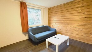 Une pièce avec un mur en bois, un canapé gris, une table blanche et une fenêtre avec des rideaux.