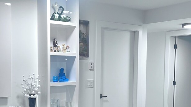 Ett modernt vardagsrum med en svart lädersoffa, vita, inbyggda hyllor med dekorativa föremål och en taklampa.
